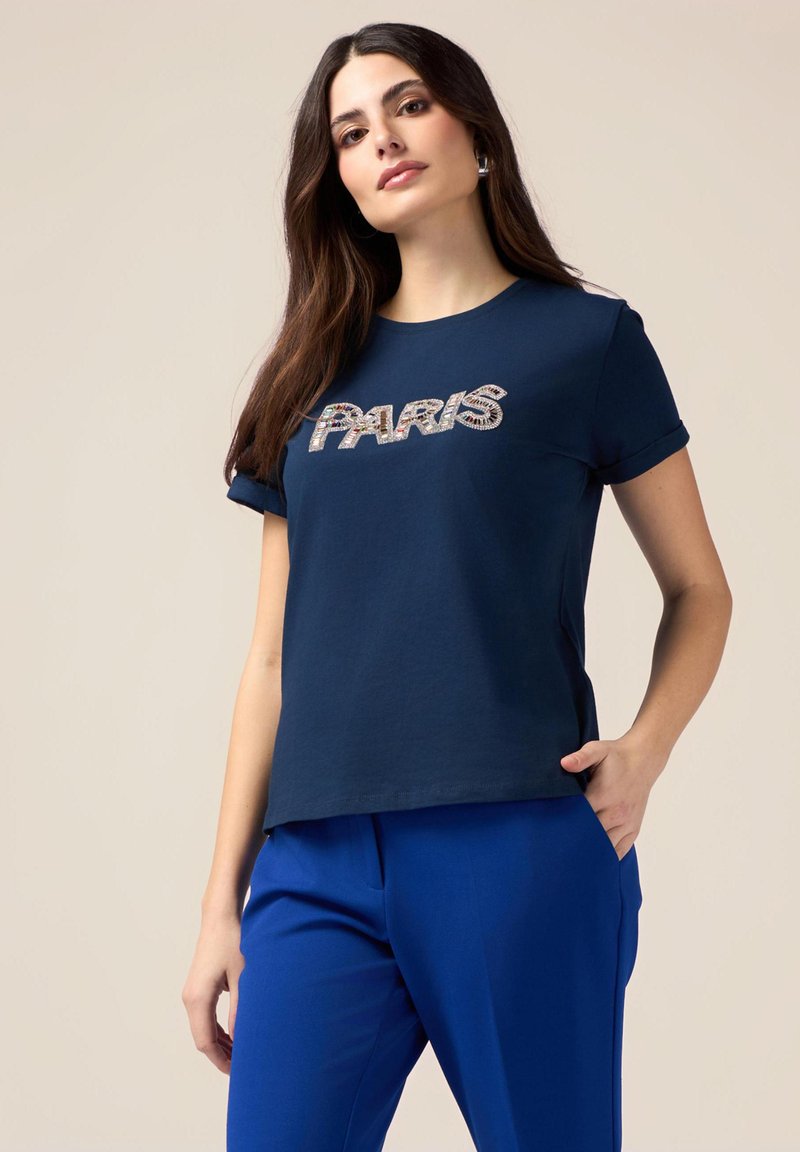 Navyblauwe katoenen T-shirt met de tekst "PARIS" in tekstuurlijke, reflecterende letters. Korte mouwen en een relaxte pasvorm, gecombineerd met blauwe broek.