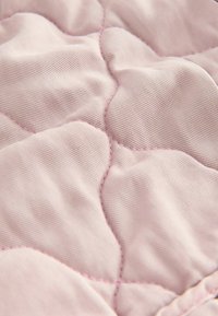 Lys pink quiltet stof med en subtil tekstur og diamantformet syning samt kontrasterende pink tråd accenter. Blød og glat overflade.