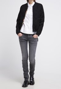 Kviltad svart bomberjacka med ett kontrasterande mönstrat foder, i kombination med grå slim-fit jeans och svarta ankelboots.