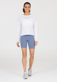 Lightweight white long-sleeve top paired with light blue fitted shorts, featuring stretchy material and flat seams. Gray sneakers complete the outfit.