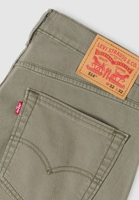 Olivgrüne Levi's 514 Jeans mit einem Lederpatch mit rotem Druck, einer abgesteppten Gesäßtasche und einem kleinen roten Logoetikett an der Seite.