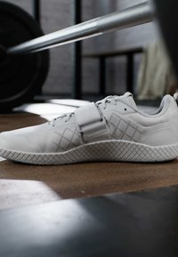 Valkoinen urheilukenkä, jossa on teksturoitu päällinen, timanttikuosiset sivut, nauhakiristys ja leveä remmi keskijalan alueella tukemista varten.