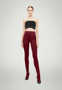 Bordeaux leggings med en glat tekstur og høj talje-design, parret med en tætsiddende sort stropløs top og sorte høje hæle.