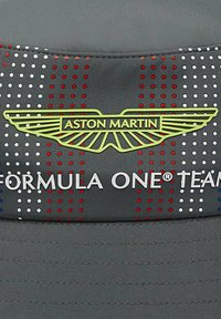 Szara czapka z logo Aston Martin w kolorze żółtym, tekst "FORMULA ONE® TEAM" w białym oraz w kropkowany wzór w czerwonym i białym. Miękka tkanina, usztywniona konstrukcja.