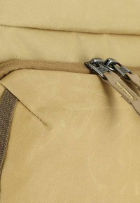 Khaki rugzakstof met een getextureerde afwerking, voorzien van een ritsvak en metalen ritshardware. Het ontwerp is functioneel en compact.