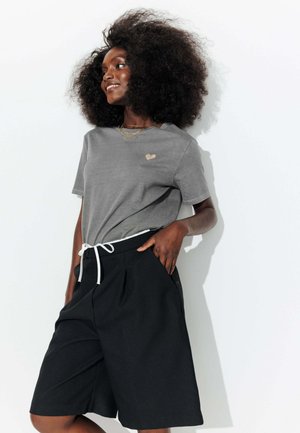 T-shirt gris à manches courtes avec un petit graphisme en forme de cœur doré, associé à un short noir plissé avec un cordon de serrage blanc et des poches.