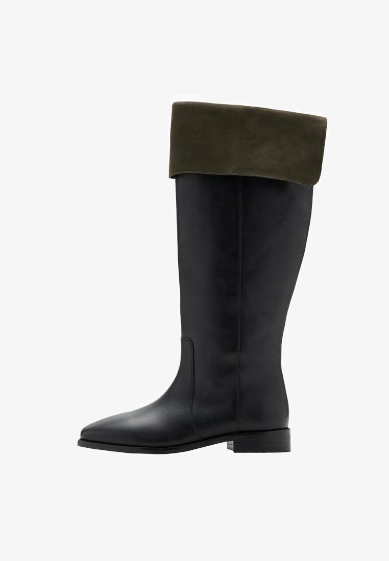 Bota de cuero negra hasta la rodilla con un puño de ante verde oscuro, punta afilada y suela plana. Líneas limpias y diseño minimalista.