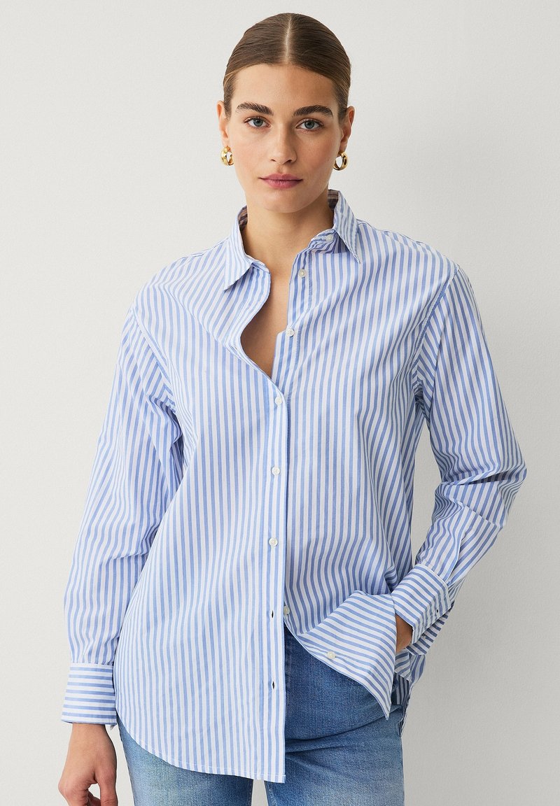 Camisa de botones a rayas azules y blancas con cuello, de mangas largas y corte relajado. Cuenta con un bolsillo en el lado izquierdo.