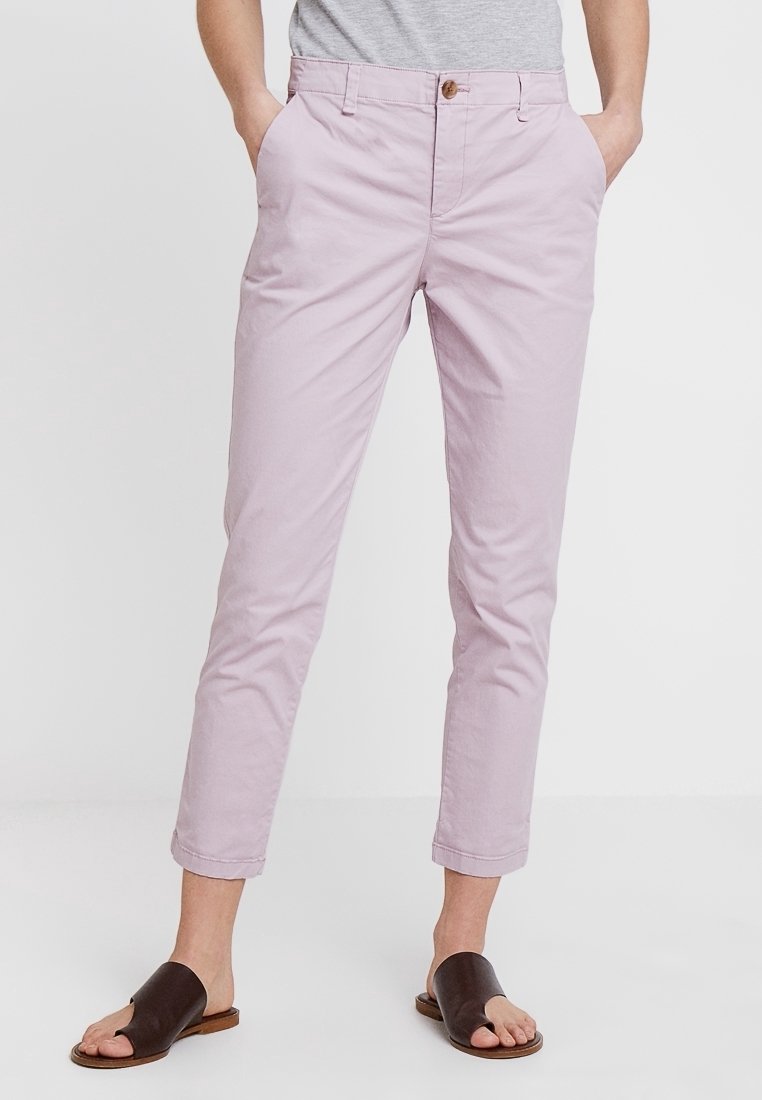 Pantalon court slim fit violet clair porté avec une chemise grise et des sandales noires ouvertes à l'avant, mains dans les poches.