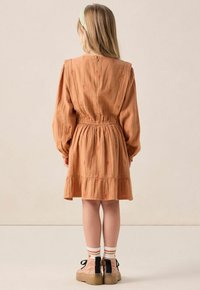 Robe couleur rouille avec taille froncée, longues manches bouffantes et ourlet volanté. Comprend des accents brodés et une fermeture à boutons à l'arrière.