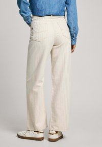 Pantalones vaqueros de pierna ancha a rayas blancas con bolsillos traseros, combinados con una camisa de mezclilla y zapatillas blancas con suela marrón y acentos de estampado de leopardo.