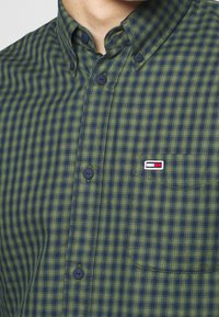 Camisa de botones a cuadros verde y azul marino, de algodón, con un bolsillo en el pecho y detalle bordado del logo, con botones oscuros y cuello con solapa.