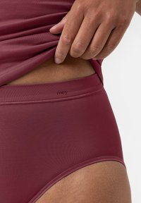 Mörkröd underkläder med medelhög midja i slät, strukturerad tyg. Har en mjuk midjeresår med subtil branding, delvis synlig under ett överlager.