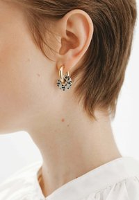 Pendientes de aro de oro con un encanto circular moteado en blanco y negro. Los pendientes presentan un acabado suave y un diseño en capas.