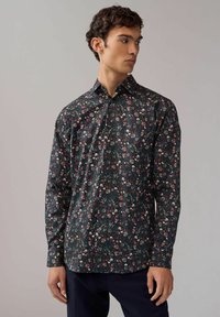Floral Hemdbluse mit langen Ärmeln aus dunkelgrünem Stoff, mit pinken und weißen Blumen, Knopfkragen und vorderer Knopfleiste.