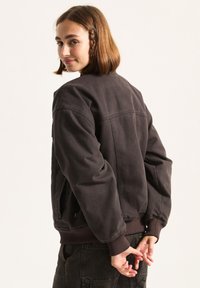 Dunkelbraune Bomberjacke mit lockerer Passform, gerippten Bündchen und Saum, seitlichen Taschen und sichtbaren nährdetails.