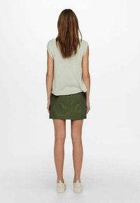 Hellgraues Kurzarmoberteil, kombiniert mit einem olivgrünen Minirock. Das Outfit wird durch beigefarbene Plateausneaker ergänzt.
