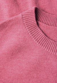 Primo piano di un morbido tessuto di maglione rosa pallido che mette in evidenza il collo a coste e la fine trama del punto.