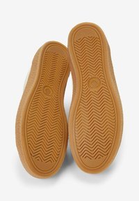 Suelas de zapatillas con un diseño de goma estampada, de color marrón claro con un acabado Texturizado, mostrando un logo circular en el arco.