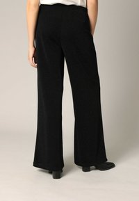 Zwarte hoge taille flared broek van textuurstof, met een gladde tailleband en wijde pijpopeningen. Platte naden zonder zichtbare hardware.