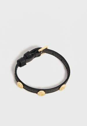 Sort læderarmbånd med tre gyldne runde nitter og en lille gylden spænde på en ensfarvet baggrund.