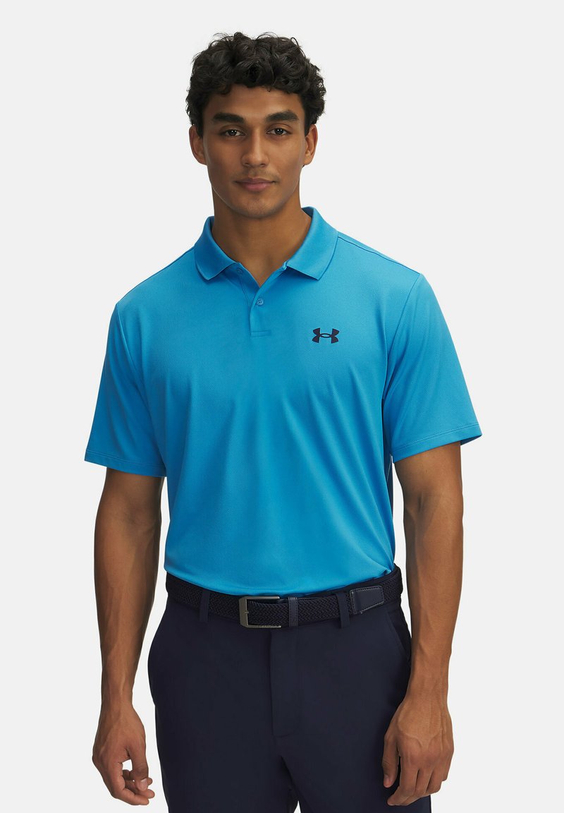 Světle modré polo tričko s límečkem a krátkými rukávy, s černým logem Under Armour na levé straně hrudi. Nosené s tmavými kalhotami.