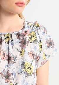 Bloemige blouse met een lichte, doorschijnende stof met pastelroze, gele en blauwe bloemenpatronen, elastische halslijn en ontspannen mouwen.