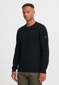 Pulover negru dintr-un material moale, tricotat. Are un guler rotund, mansete și tiv din tricot, cu un mic patch cu logo pe mâneca stângă.