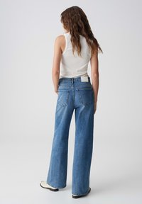 Uitlopende blauwe denim jeans met een hoge taille, vijf-pocket ontwerp en een wit label op de achterkant, gestyled met een aansluitend wit tanktop.