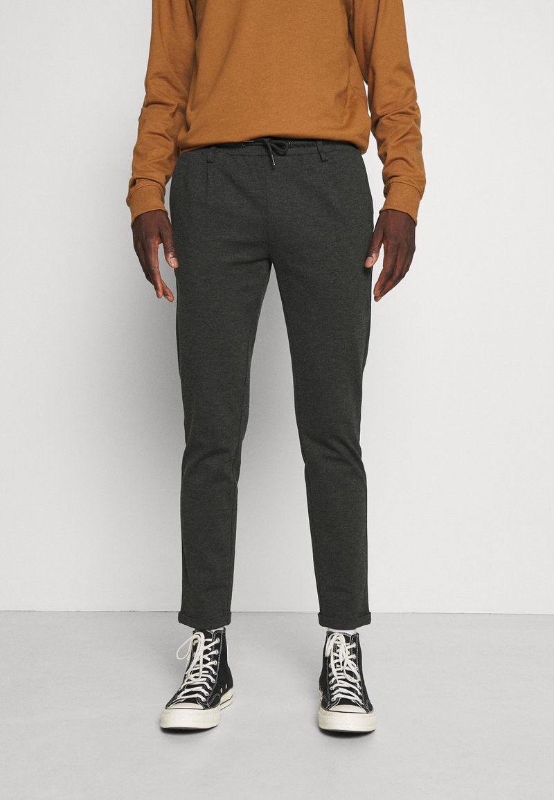 Mørkegrå tapered bukser med elastisk talje og snoretræk, parret med sorte high-top sneakers. Stof ser blødt og glat ud.