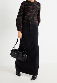 Black denim maxi skirt, knitted multicolored sweater, and a glossy black handbag with zippers and a strap. Pointed black heeled boots.