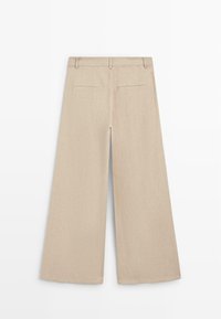 Beige pantalon met brede pijpen, riemlussen en twee achterzakken met een sierbies, plat liggend vanuit de achterkant tegen een witte achtergrond.