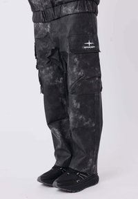 Schwarze Cargo-Hosen mit einem strukturierten, verblassten Muster, elastischem Bund, seitlichen Taschen und einem weißen Logo am Bein, kombiniert mit schwarzen Sneakern.