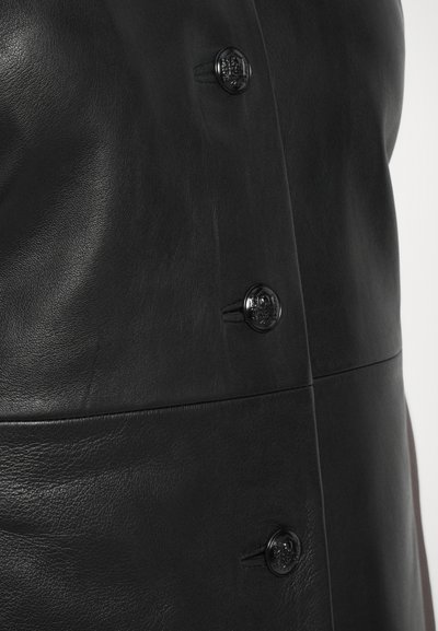 Czarna skórzana kurtka z gładką teksturą, wyraźnymi szwami i okrągłymi czarnymi guzikami z wytłoczonymi detalami.