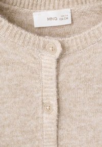 Bež pletena jopica z rebrastim ovratnikom, dvema gumboma in mehko teksturo. Na vratu je vidna etiketa za nego. Velikost: 3-4; dolžina: 104 cm.