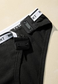 Black cotton underwear with a white elastic waistband featuring the text "NEXT." Includes two black plastic tab closures and flat seams.