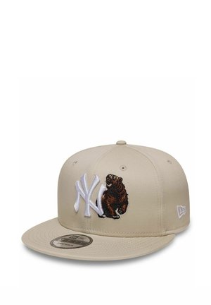 Cappellino da baseball beige con logo NY bianco e orso marrone ricamato sul davanti, visiera piatta e logo New Era sul lato.