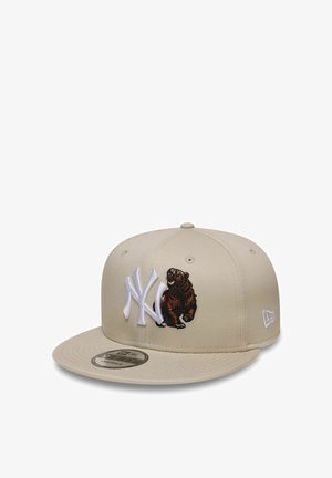 Cappellino da baseball beige con logo NY bianco e orso marrone ricamato sul davanti, visiera piatta e logo New Era sul lato.