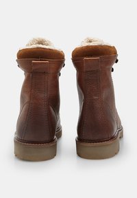 Pár hnedých kožených zimných čižiem s béžovým kožúškom a gumovými podrážkami, zobrazené zozadu na bielom pozadí.