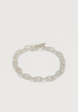 Pulsera delicada hecha de pequeñas cuentas de plata unidas formando eslabones en forma de lazos, con un cierre de palanca sobre un fondo blanco.