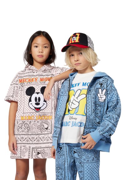 Twee kinderen in bijpassende outfits met Mickey Mouse. Het meisje draagt een roze jurk met bandana-patroon; de jongen heeft een blauwe hoodie en broek aan.