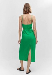 Vestido de satén verde con corte en la espalda, tirantes finos ajustables, un corsé ceñido y una abertura en la pierna en la parte trasera. Textura suave, hasta la mitad del muslo.