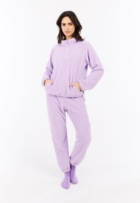 Fialový fleece relaxačný set s textúrovaným vzorom; obsahuje zapínací golier, bočné vrecká a elastické manžety, doplnené o zodpovedajúce ponožky.