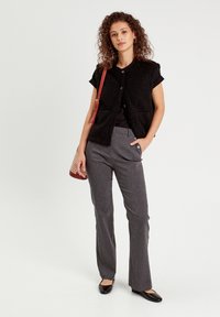 Gilet texturé noir à manches courtes, associé à un pantalon évasé gris. Sac à épaule marron avec des accents tissés, chaussures plates noires.