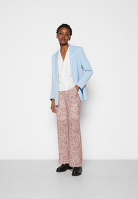 Blazer azul-claro sobre uma blusa branca, combinado com calças largas de padrão floral em vermelho e tons pastéis. Sapatos pretos completam o visual.