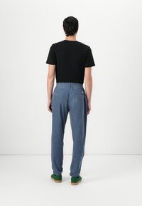 T-shirt noir, coupe relax, associé à un pantalon bleu à taille élastique avec une texture subtile et des poches arrière. Des chaussures vertes complètent la tenue.