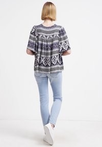 Top a righe bianco e nero con maniche corte, vestibilità comoda e scollatura rotonda, abbinato a jeans skinny azzurri e sneaker bianche.