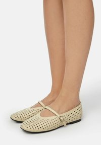 Bailarinas de piel beige con patrones florales troquelados, correa estrecha en el empeine y suelas negras bajas.
