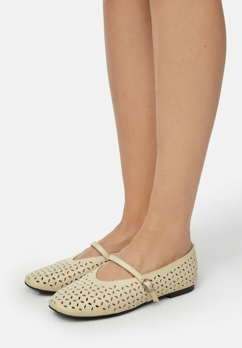 Bailarinas de piel beige con patrones florales troquelados, correa estrecha en el empeine y suelas negras bajas.