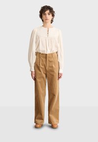 Off-white long-sleeve blouse with a rounded neckline and button placket, paired with beige corduroy wide-leg trousers and wooden clogs.
